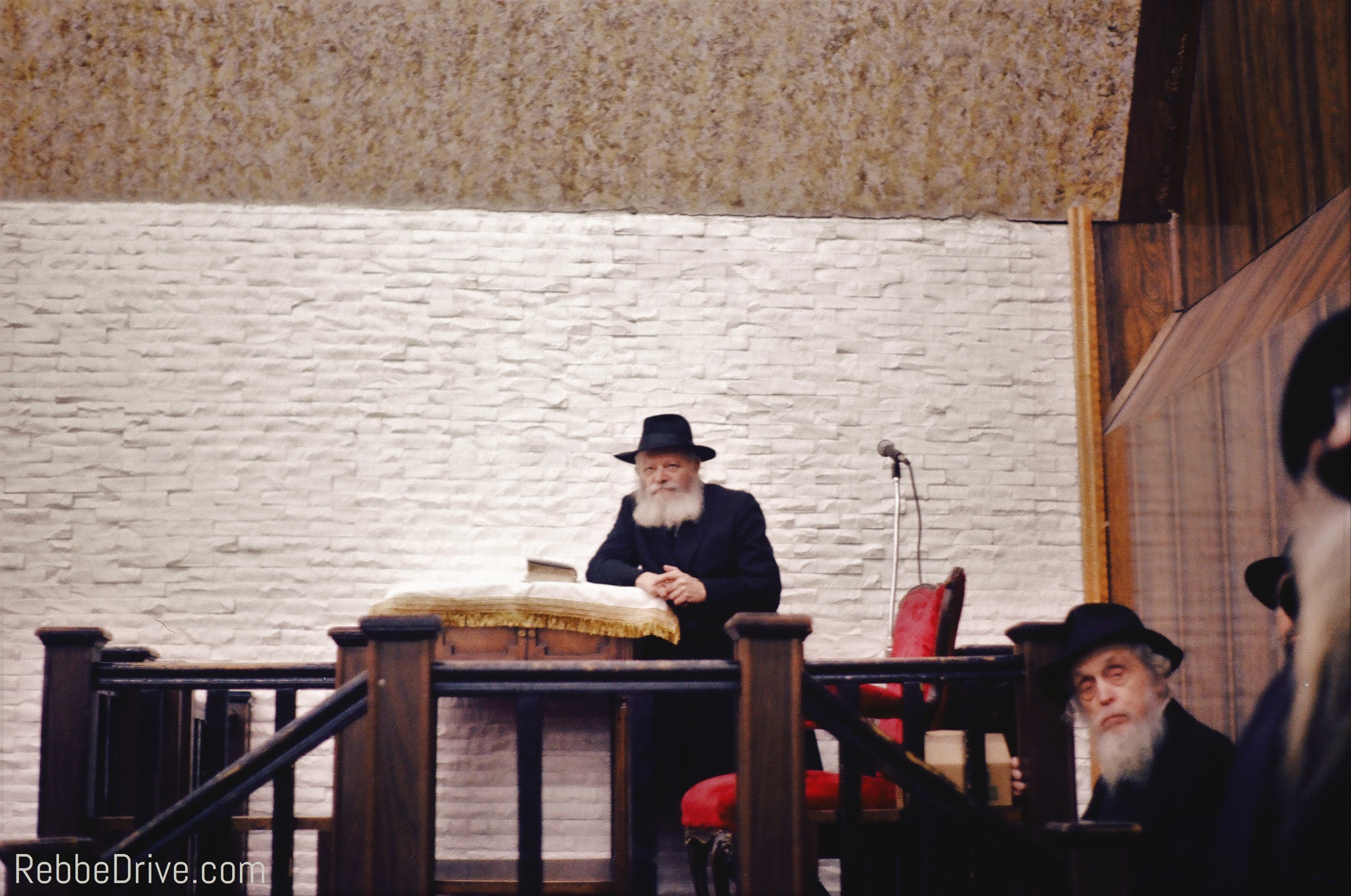 The Lubavitcher Rebbe seated before an open sefer at a children’s rally in 770.